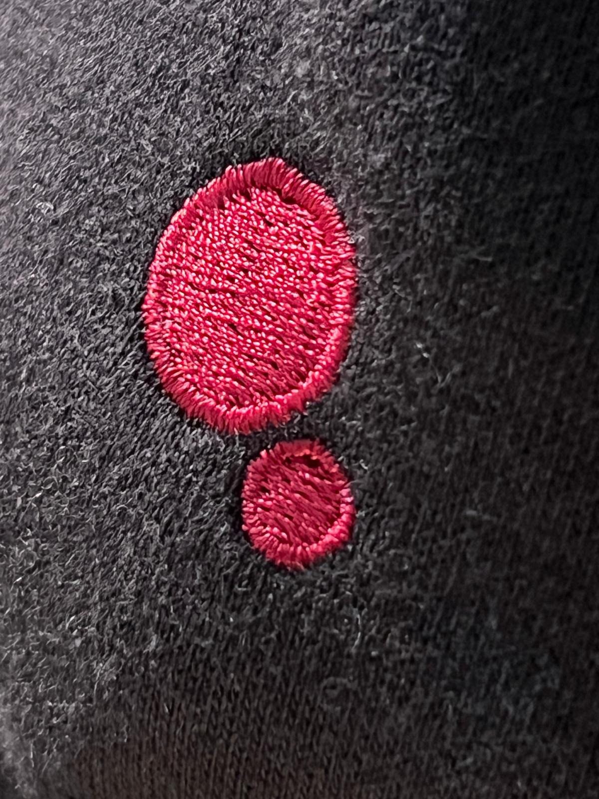 Close-up of the embroidered red double-dot mark stitched into black heavyweight fleece