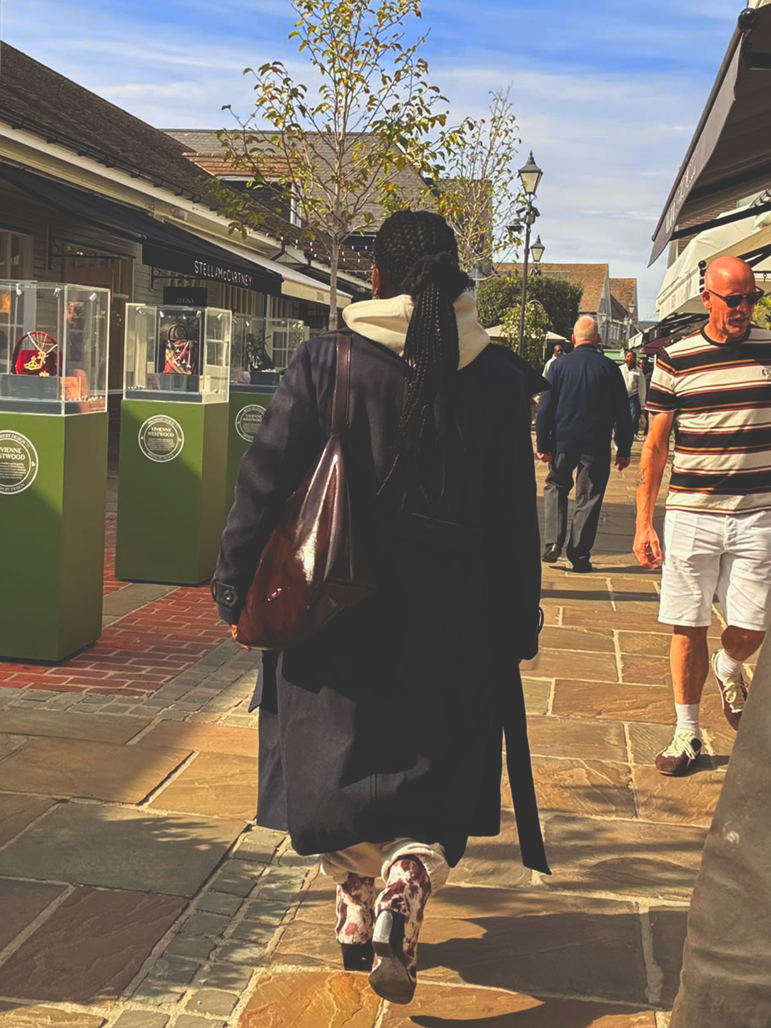Model walking away in a long navy coat with a burgundy leather bag, the cream hood showing at the collar
